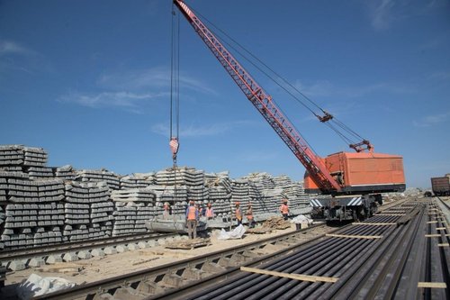Ground imagery of a DMR construction site featuring the large red crane and stacks of concrete rail ties. Imagery via KTZ official Telegram Channel.