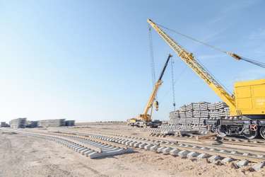 Ground imagery of a DMR construction site featuring the large yellow crane, stacks of concrete rail ties, and freshly laid track to facilitate supply transport. Imagery via KTZ official Telegram Channel.