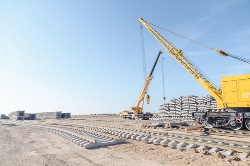 Ground imagery of a DMR construction site featuring the large yellow crane, stacks of concrete rail ties, and freshly laid track to facilitate supply transport. Imagery via KTZ official Telegram Channel.